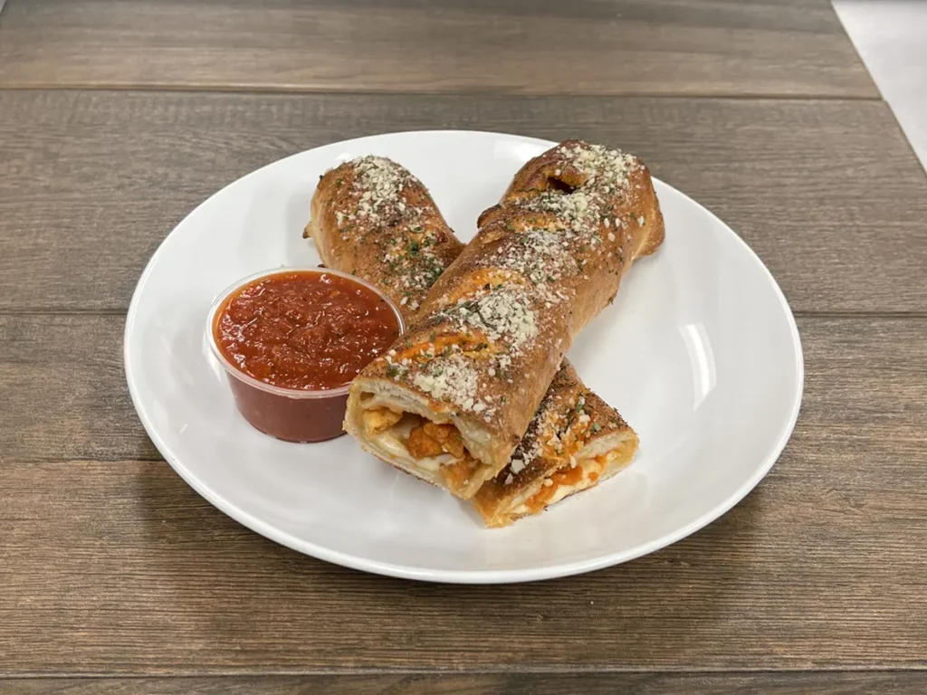 Buffalo chicken roll cut in half with a cup of marinara sauce