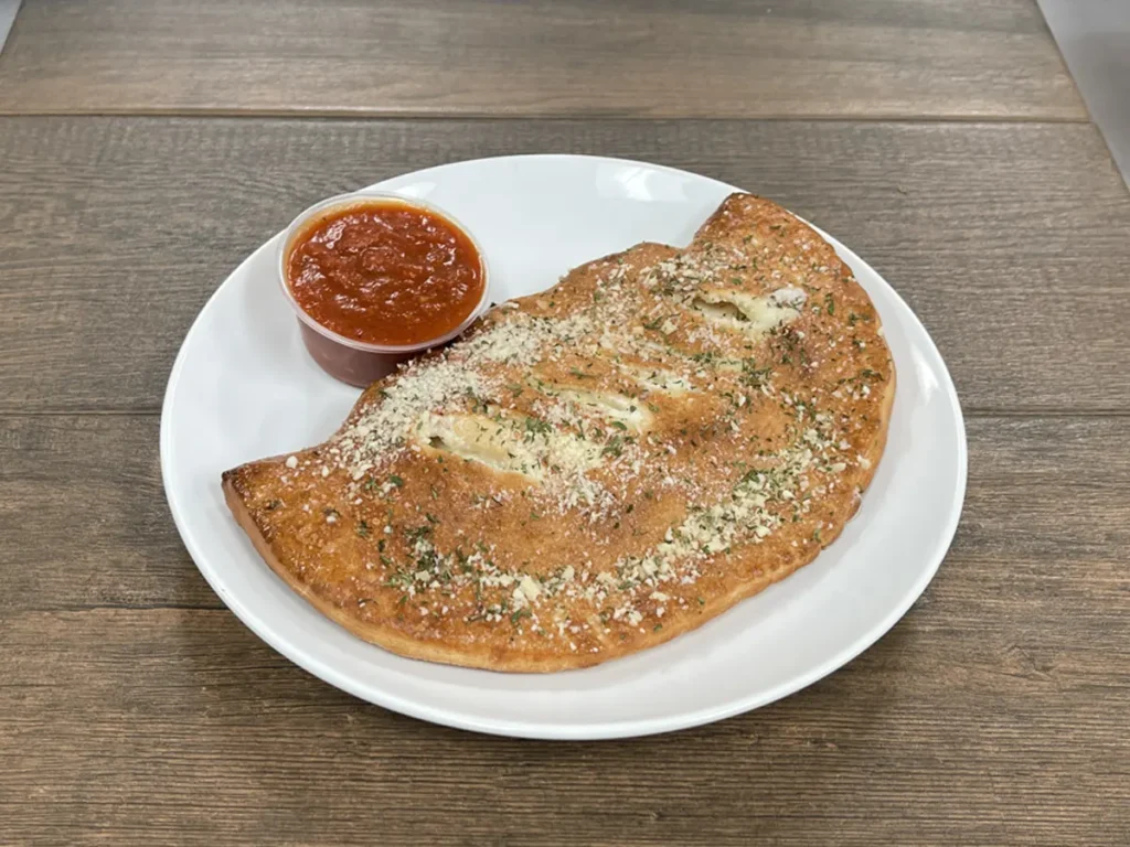 Golden baked calzone with a cup of marinara sauce