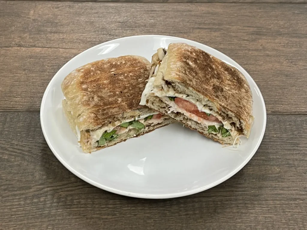 Pressed chicken caprese panino with tomato, basil and fresh mozzarella, cut in half
