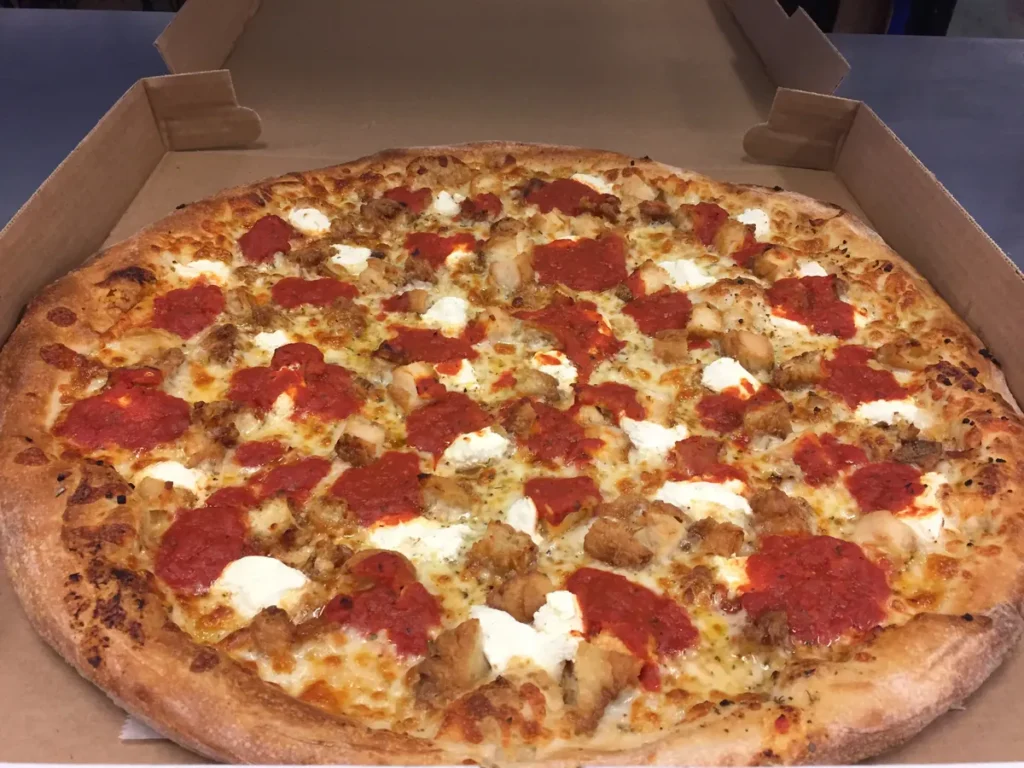 Chicken parm pizza with breaded chicken, ricotta and dollops of marinara on a white base