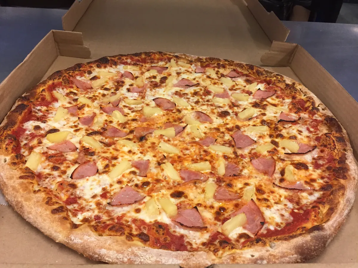 Hawaiian pizza topped with Canadian bacon and pineapple in an open pizza box