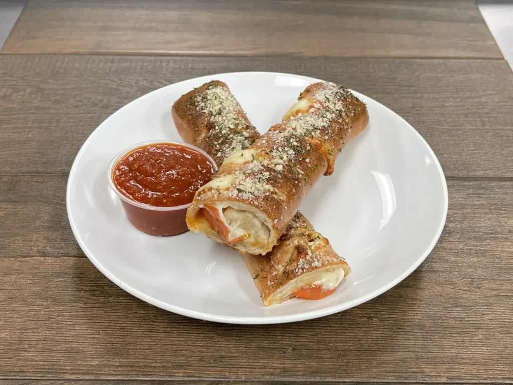 Pepperoni roll cut in half with a cup of marinara sauce